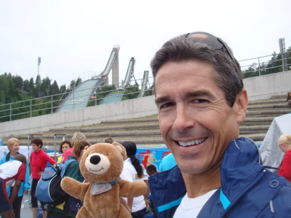 Man holding teddy bear with ski jumps in the background