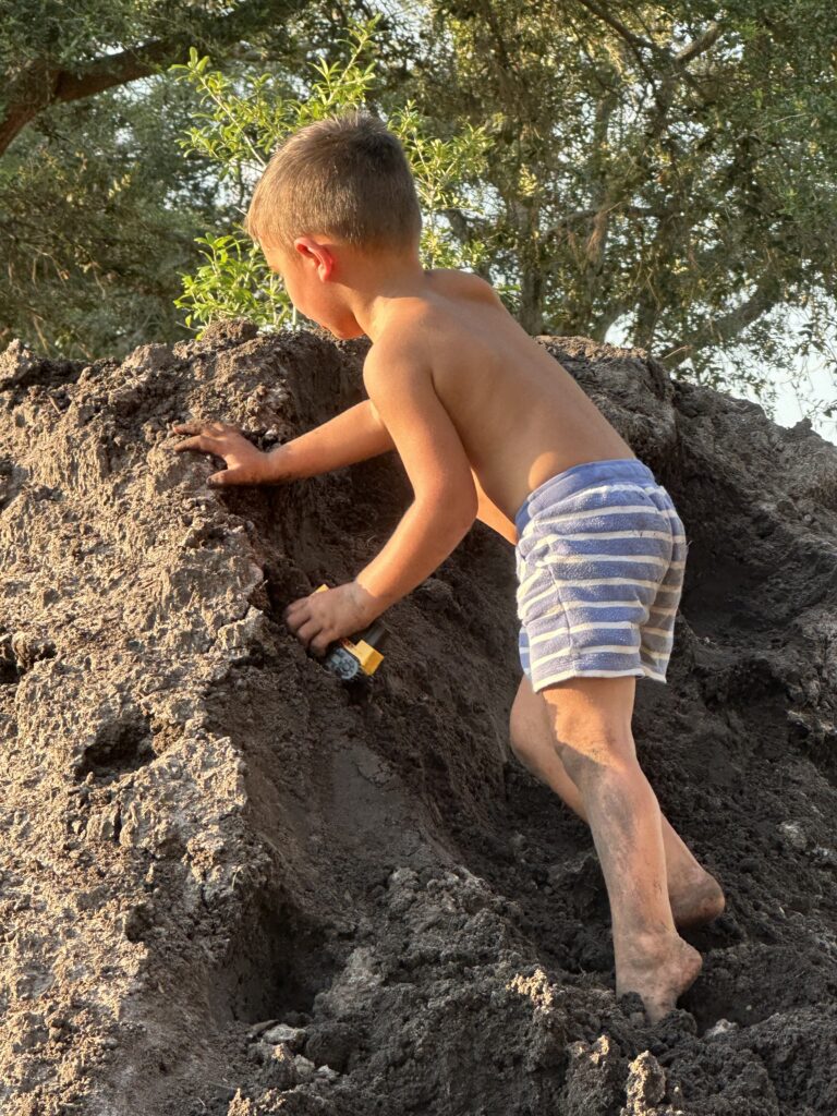 A three year old boy playing on a dirt pile