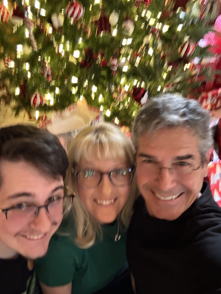 Three people sitting by Christmas tree 